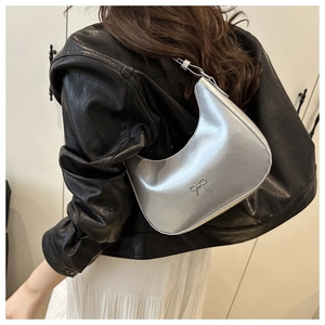 Detail of silver metallic hobo bag with bow buckle worn over a black leather jacket