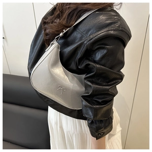 Detail of a silver crescent-shaped shoulder bag in glossy patent leather with bow accent