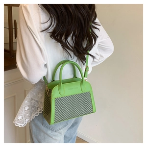 Detailed close-up of green herringbone weave texture and embossed leather on the crossbody bag