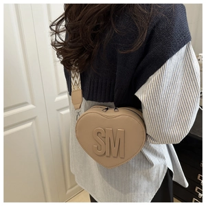 Close-up of khaki heart-shaped bag with embossed SM logo and patterned wide strap