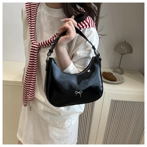 Close-up of black patent leather underarm bag featuring a silver metal bow detail