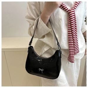 Detail of glossy black patent leather shoulder bag with a silver bow metal accessory