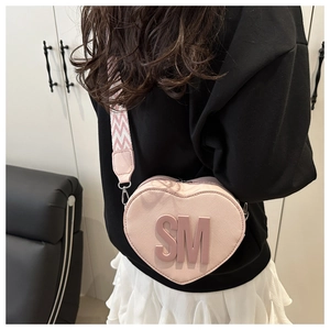 Detail of pink heart crossbody bag with textured leather and wide woven strap on model