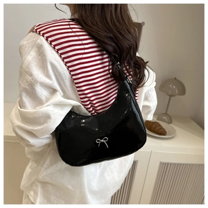 Detail of black patent leather hobo bag with a silver metallic bow on minimalist strap