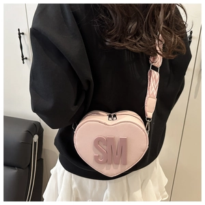 Pink heart-shaped crossbody bag with SM logo and woven strap shown on a model