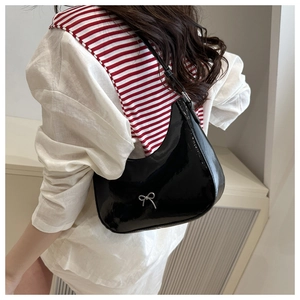 Detail of black glossy patent leather shoulder bag featuring a silver bow metal buckle
