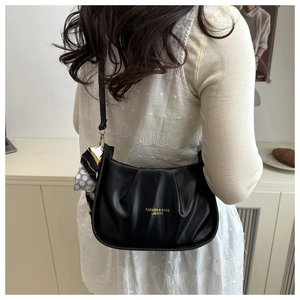 Détail d'un sac à bandoulière noir plissé avec un charm en soie à motifs pois élégants