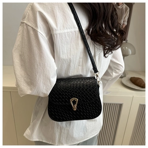 Close-up of black woven texture crossbody bag with gold stirrup buckle on a model