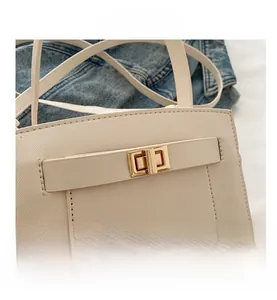 Macro shot of gold twist lock closure and crossgrain leather detail on cream handbag