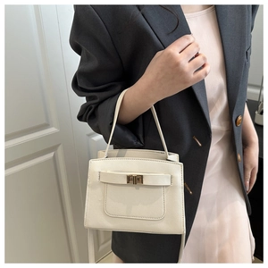 Detail of cream crossbody bag with golden turn-lock clasp and stylish top handle on model