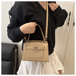 Detailed view of beige crossbody bag featuring golden turn-lock and leather strap decor