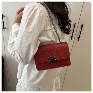 Red woven leather crossbody bag with silver chain strap worn by model on white background