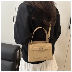 Crossbody view of a beige faux leather handbag with metal turn-lock on a female model