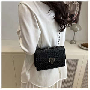 Detail of silver chain strap and metal lock on a black crocodile texture crossbody bag