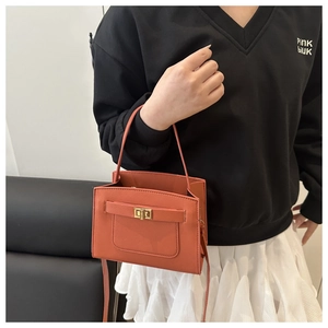 Detail of orange Saffiano leather crossbody bag with gold-tone rotating lock on textured background