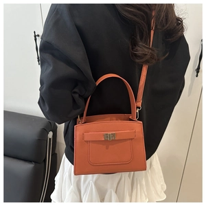 Detail shot of orange Saffiano leather crossbody bag with golden twist lock on a model