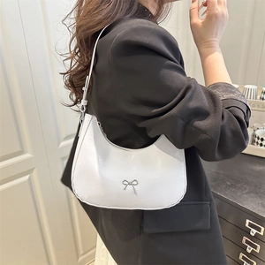 White crescent hobo bag with silver bow detail worn by a model in black blazer