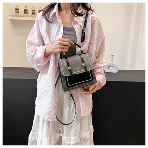 Detail of grey and black crossbody bag showing top handle and gold metal hardware buckles