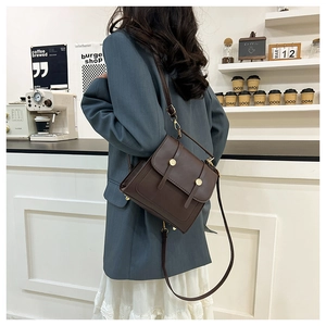 Dark brown vintage crossbody bag with gold round buckles shown on a model in a cafe