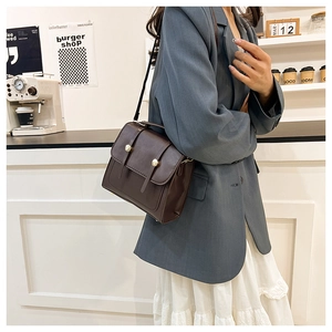 Detailed view of a dark brown vintage crossbody bag with metal magnetic buckles in a cafe