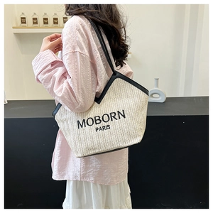 Detail of woven straw tote bag with black MOBORN PARIS embroidery and contrasting shoulder strap