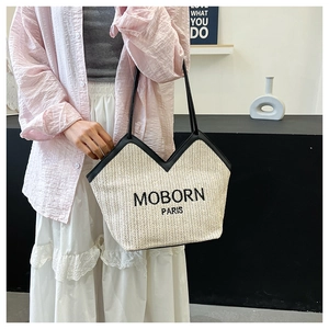 Detail of woven straw tote bag with black leather trim and MOBORN PARIS embroidery