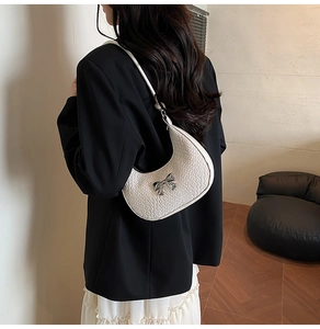 Close-up of white crocodile pattern crescent bag with silver bow on woman's shoulder