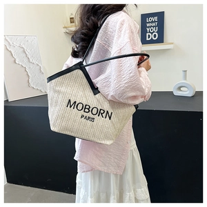 Detail of a beige woven tote bag with black trim and MOBORN PARIS branding on a model