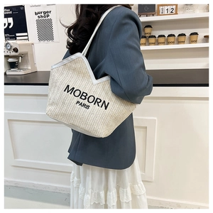 Detail view of woven straw tote bag featuring white leather trim and contrast logo