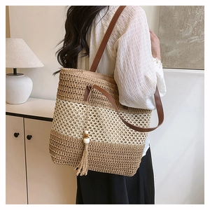 Détail d'un sac cabas tissé en paille avec bandoulière en cuir brun et pompon déco