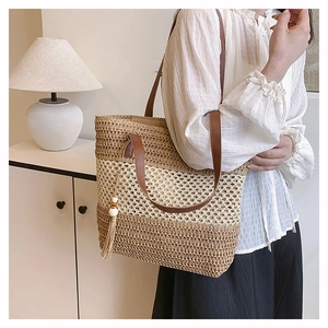 Close-up of woven straw tote bag with brown leather handles and wooden bead tassels
