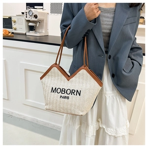 Detail of woven straw tote bag with brown leather trim and MOBORN PARIS logo on front