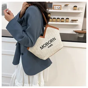 Detalle del bolso tote de paja tejida con ribete de cuero marrón y logo MOBORN PARIS