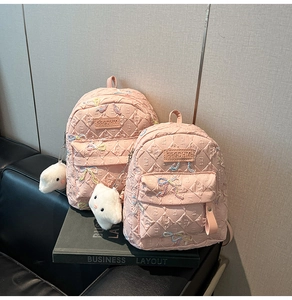 Detail of pink quilted nylon backpacks with colorful bow embroidery and cat plushies