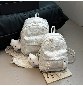 Detail of white quilted backpacks with embroidered bows and plush cloud keychain charm