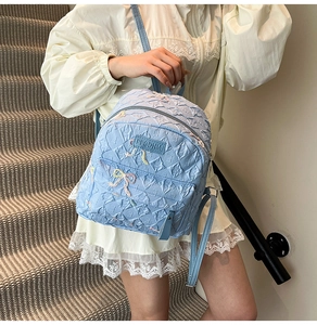 Detailed view of light blue backpack with bow decoration and pleated texture on model