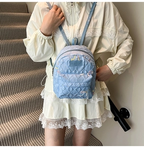 Close-up of light blue quilted mini backpack with floral embroidery and E pattern