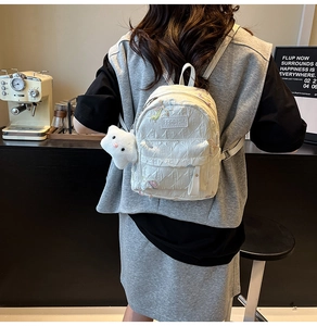 Detail of white quilted backpack featuring colorful butterfly embroidery and plush cat charm