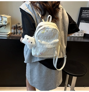 Close-up of white quilted mini backpack with colorful bow embroidery and plush charm