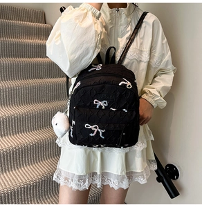 Detail of black backpack with colorful bow embroidery and white plush kitten pendant