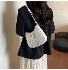 Close-up of a white leather underarm bag featuring silver eyelets and a wide buckle strap