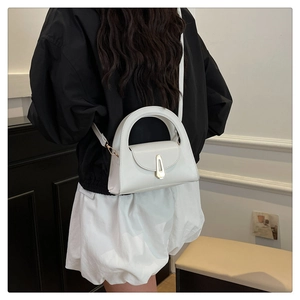 Detail of white leather handbag with golden shield-shaped metal lock and arched handle