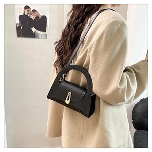 Detail view of a black minimalist handbag with a unique gold buckle on a model's shoulder