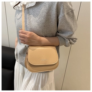 Close-up of beige crossbody bag featuring elegant flap cover and fashion trend lettering