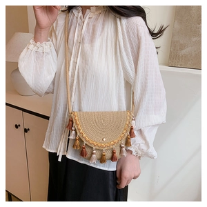 Détail du sac coquillage tissé beige avec pompons frangés et broderie ondulée sur le rabat