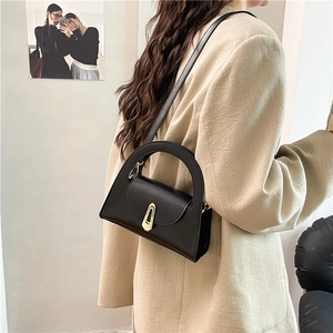 Minimalist black leather half-round handbag with gold clasp worn by a model in a beige blazer