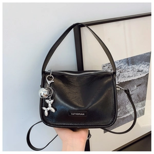 Details der glänzenden schwarzen Ledertasche mit silbernen Beschlägen und Ballonhund-Anhänger