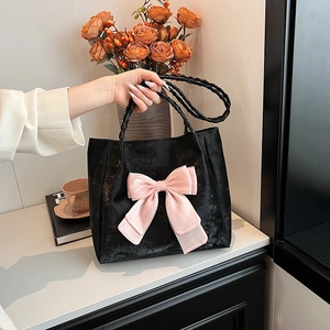 Elegant black tote bag with pink bow and woven handles in a lifestyle setting