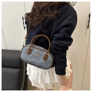 Denim Boston bag with leather trim and gold hardware styled on a model in home setting