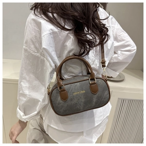 Detail of grey denim bowling bag with brown leather handles and gold metal hardware